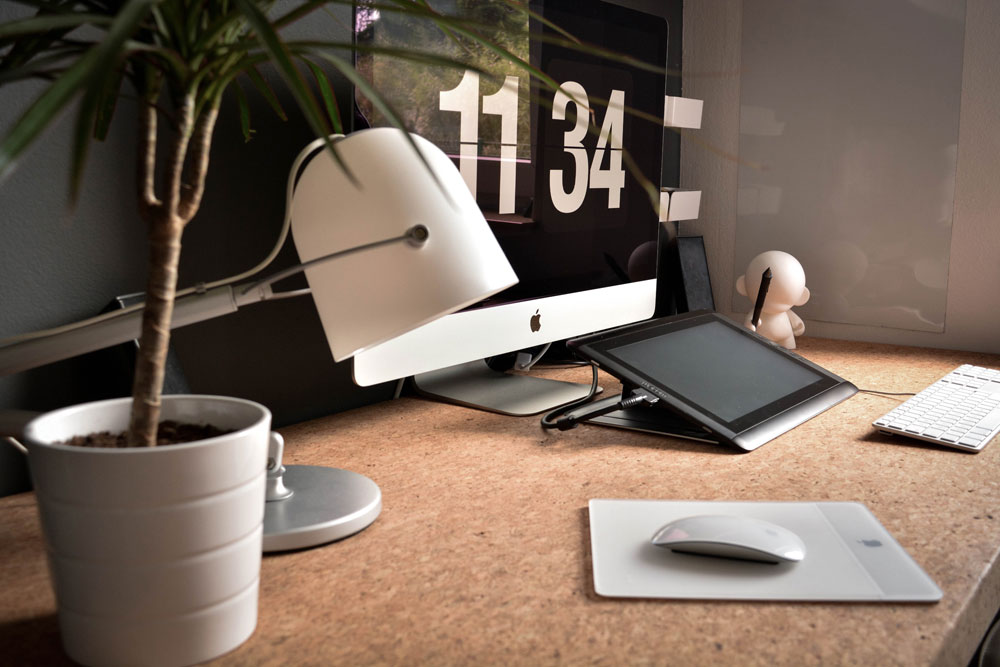 Office space with a Mac computer, lamp, tablet, mousepad, keyboard, and plant