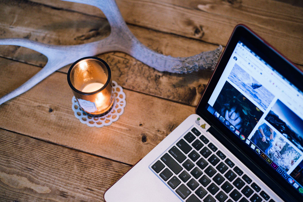 A display modern and a lit candle and an antler on a table next to a laptop