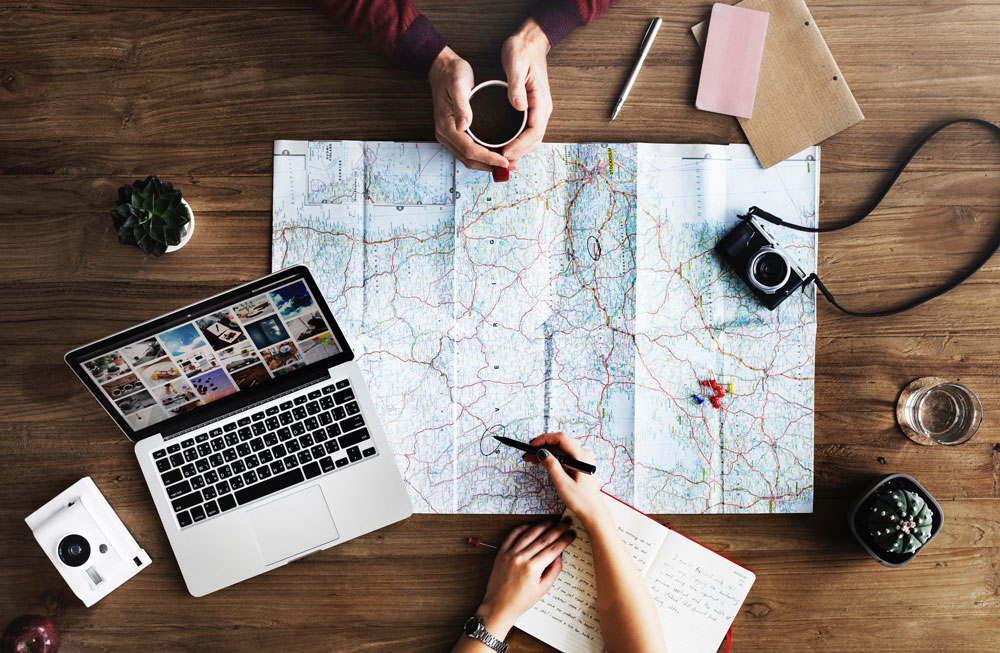 An overhead shot of two people planning a trip with a map and a laptop